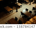 Wooden tables and chairs stand empty on a tiled outdoor terrace under warm evening lights in Mostar, Bosnia and Herzegovina. Quiet nighttime atmosphere of an outdoor cafe after closing hours 138784147