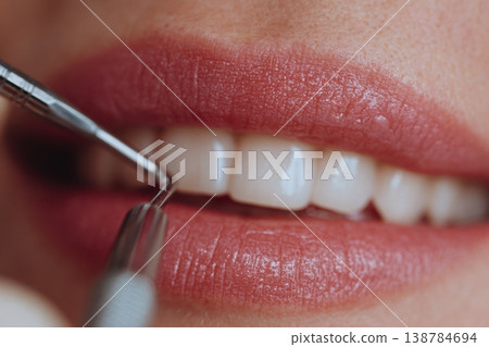 A patient sits in a dental chair while a dental hygienist uses a tool to clean their teeth and check for any issues 138784694