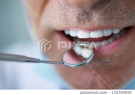 A dentist looks inside a patients mouth using a small mirror while standing in a dental clinic during a check-up A dentist looks inside a patients mouth using a small mirror while standing in a dental clinic during a check-up 138784695