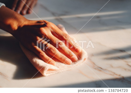 A hand is seen wiping a surface with a cloth in warm natural light during a cleaning session in the afternoon 138784720
