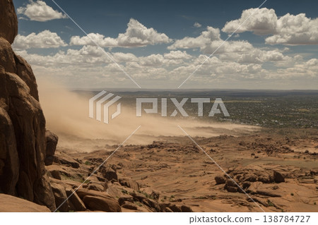 A dust storm rises in the distance while clouds form in the blue sky above rocky hills in a desert location during the afternoon A dust storm rises in the distance while clouds form in the blue sky above rocky hills in a desert location during the afternoon 138784727