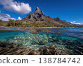 Fish swim in clear water near rocks below a mountain in Tahiti under a bright blue sky. The scene shows nature and water life 138784742
