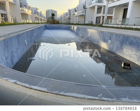 Empty swimming pool reflecting modern residential buildings and clear sky background 138784818