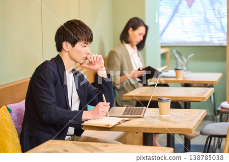 A man and a woman working on their laptops in a cafe-style co-working space. 138785038