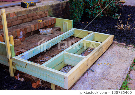 Construction of wooden frame for steps by brick wall in garden setting 138785400