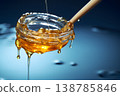 honey drizzling from a wooden dipper into a glass jar on a reflective surface in soft lighting 138785846