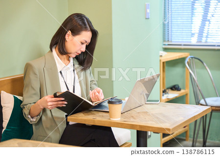 A businesswoman working on her PC while checking her planner in a cafe-style office. A businesswoman working on her PC while checking her planner in a cafe-style office. 138786115
