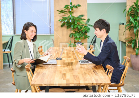 Business professionals, a man and a woman, chatting over coffee in a free-address office. 138786175