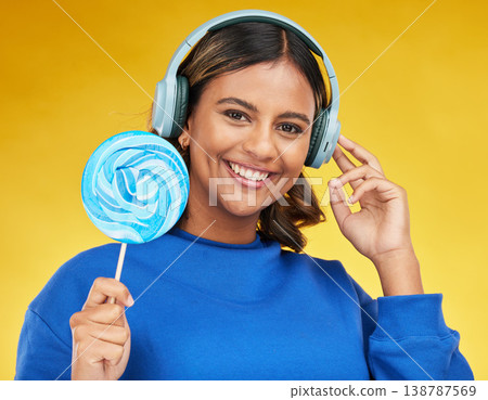 Woman, lollipop and headphones in studio portrait, smile or choice for radio, podcast or music by yellow background. Happy gen z girl, student and candy with streaming subscription, sugar and fashion 138787569