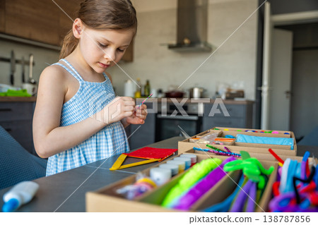 Little girl decorating handmade craft with colorful self adhesive rhinestones at table. Kids creativity fine motor skills development and learning through play concept. 138787856