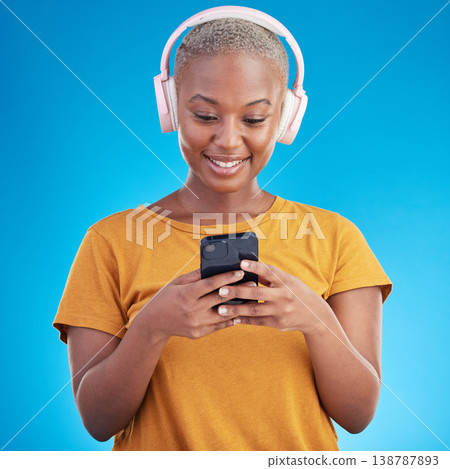 Woman, smartphone and headphones listening to music, audio streaming service or social media on blue background. Young african person or influencer chat on mobile for podcast subscription in studio Woman, smartphone and headphones listening to music, audio streaming service or social media on blue background. Young african person or influencer chat on mobile for podcast subscription in studio 138787893
