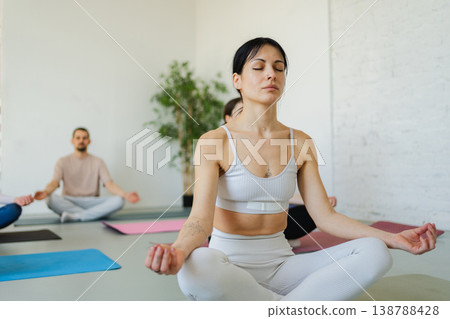 Yoga mindfulness meditation. Group of sporty people doing exercise in studio for class for yoga wellness mindfulness meditation. Men women practicing yoga sitting in lotus pose meditating relaxing Yoga mindfulness meditation. Group of sporty people doing exercise in studio for class for yoga wellness mindfulness meditation. Men women practicing yoga sitting in lotus pose meditating relaxing 138788428