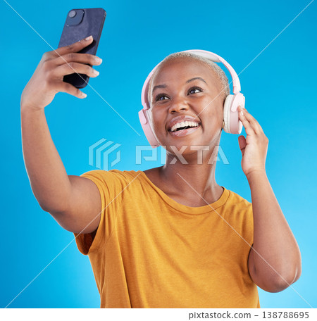 Woman, selfie and headphones listening to music, audio streaming and social media influencer on blue background. Young african person on mobile video call and profile picture or photography in studio Woman, selfie and headphones listening to music, audio streaming and social media influencer on blue background. Young african person on mobile video call and profile picture or photography in studio 138788695