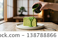 A scene of pouring a rich sauce over a matcha chiffon cake, evoking the image of a modern Japanese cafe. 138788866