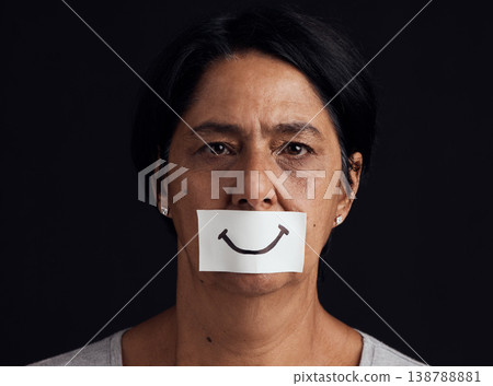 Portrait, fake smile or abuse and a mature woman in studio on a dark background with an expression. Depression, anxiety and mental health with a female person looking brave to hide her emotions 138788881