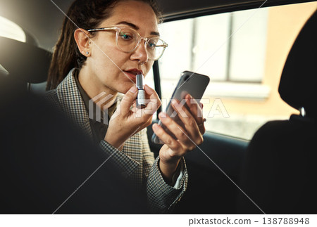 Phone, lipstick and a business woman in a car to travel in the city for work while multitasking. Face, mobile and makeup with a young female employee in a taxi or cab as a passenger for transport Phone, lipstick and a business woman in a car to travel in the city for work while multitasking. Face, mobile and makeup with a young female employee in a taxi or cab as a passenger for transport 138788948