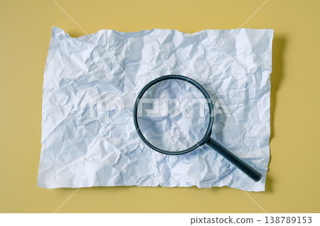 A magnifying glass over crumpled paper on color background. A magnifying glass over crumpled paper on color background. 138789153