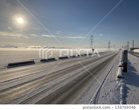 A single road cuts through a snow-covered plain and the winter sun. A single road cuts through a snow-covered plain and the winter sun. 138789346