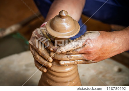 Skilled artisan hands shaping wet clay on a spinning potter wheel, creating a ceramic vase in a traditional pottery workshop. 138789692