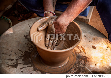 Skilled artisan hands shaping wet clay on a spinning potter wheel, creating a ceramic vase in a traditional pottery workshop. Skilled artisan hands shaping wet clay on a spinning potter wheel, creating a ceramic vase in a traditional pottery workshop. 138789693