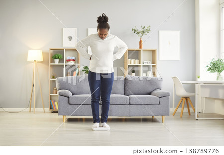 Upset fat young woman measuring her weight standing on scales in the living room at home. Upset fat young woman measuring her weight standing on scales in the living room at home. 138789776