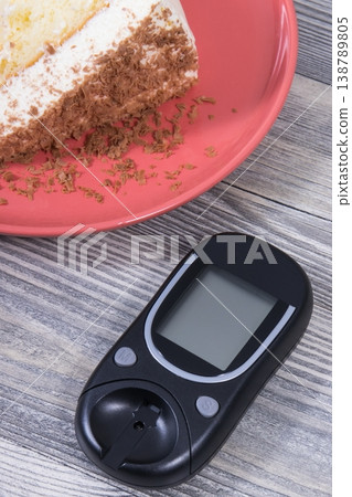 Glucose meter for measuring sugar level and piece of sweet cake with chocolate Glucose meter for measuring sugar level and piece of sweet cake with chocolate 138789805