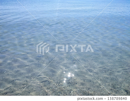 Clean transparent water on shallow sandy seashore with shells with shells on sunny summer day. Sun glare on surface of water. Small waves on sea coast. Nature backdrop. Natural background 138789840