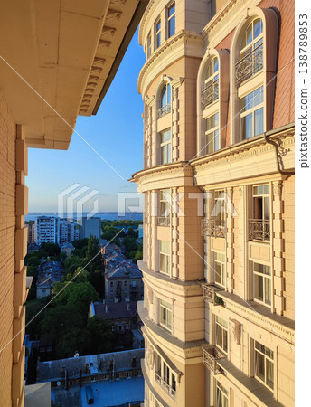 Cityscape with sea and blue sky on summer evening and sunlight illuminated white wall with windows of multi-story residential building. Old buildings, roofs, green trees. Front facade. Architecture Cityscape with sea and blue sky on summer evening and sunlight illuminated white wall with windows of multi-story residential building. Old buildings, roofs, green trees. Front facade. Architecture 138789853