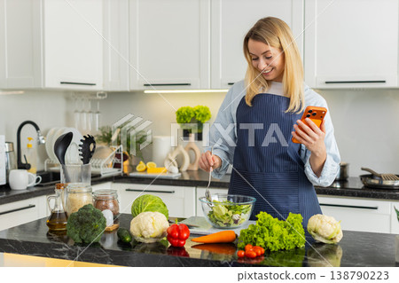Young woman checking orange smartphone recipe then preparing fresh salad for keto diets in kitchen Young woman checking orange smartphone recipe then preparing fresh salad for keto diets in kitchen 138790223