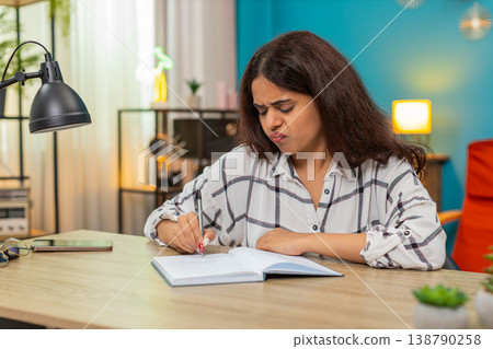 Indian woman writes in notebook crosses out lines then retries searching solution focused determined Indian woman writes in notebook crosses out lines then retries searching solution focused determined 138790258