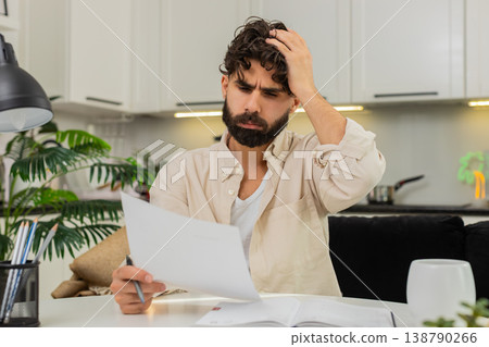 Indian man reading official letter facepalm stressed about finances writing action plan in notebook 138790266