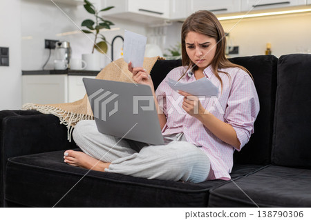 Young woman with laptop sorts utility bills and work invoices nervous and focused on budget review 138790306