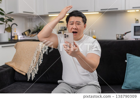 Asian man loses game on smartphone sighs in defeat frowns at bad news and shares reply in chat sad 138790309