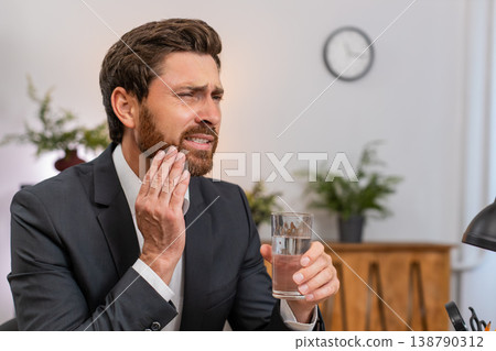Middle-aged businessman drinks cold water winces tooth pain urgently searches dentist via smartphone Middle-aged businessman drinks cold water winces tooth pain urgently searches dentist via smartphone 138790312