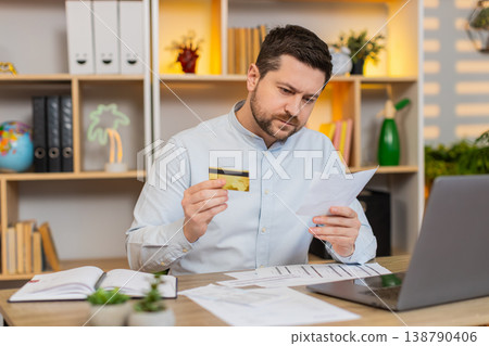 Young man on home table reviewing card and documents on laptop planning budget after recent expenses Young man on home table reviewing card and documents on laptop planning budget after recent expenses 138790406