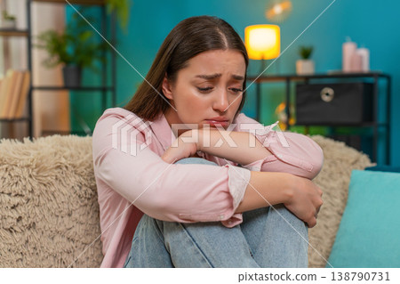 Young woman knees to chest on sofa overwhelmed by anxiety heartbreak and bankruptcy feeling apathy Young woman knees to chest on sofa overwhelmed by anxiety heartbreak and bankruptcy feeling apathy 138790731