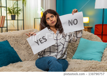 Indian woman hesitates holding yes and no signs displaying decision doubt confusion needing answer Indian woman hesitates holding yes and no signs displaying decision doubt confusion needing answer 138790757