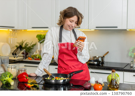 Young woman using smartphone while cooking healthy vegetables in kitchen for daily meal prep at home 138790760