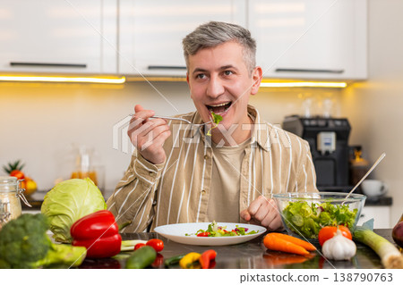 Middle-aged man enjoying fresh vegetable salad in kitchen for balanced nutrition and healthy eating Middle-aged man enjoying fresh vegetable salad in kitchen for balanced nutrition and healthy eating 138790763