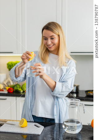 Young woman squeezing lemon into water tumbler in kitchen for fresh vitamin hydration morning habit Young woman squeezing lemon into water tumbler in kitchen for fresh vitamin hydration morning habit 138790787