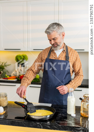 Middle-aged man pouring raw omelet mix into frying pan in home kitchen for healthy diet breakfast. Middle-aged man pouring raw omelet mix into frying pan in home kitchen for healthy diet breakfast. 138790791