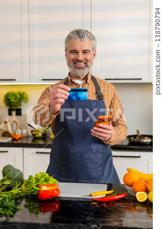 Middle-aged man uses smartphone with credit card in kitchen buying healthy groceries for diet plan Middle-aged man uses smartphone with credit card in kitchen buying healthy groceries for diet plan 138790794