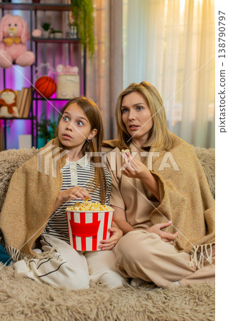 Child girl kid with mother watching cartoon together at home on sofa under warm blanket in room Child girl kid with mother watching cartoon together at home on sofa under warm blanket in room 138790797