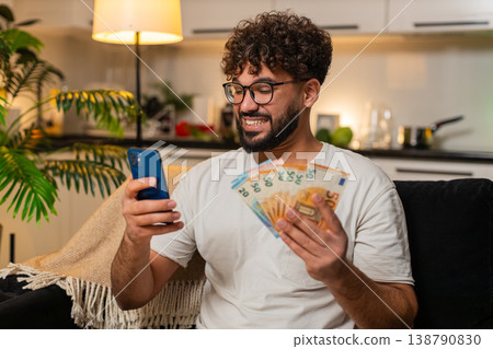 Arabian man counts euro cash using smartphone notes salary budget writes amounts in phone at night Arabian man counts euro cash using smartphone notes salary budget writes amounts in phone at night 138790830
