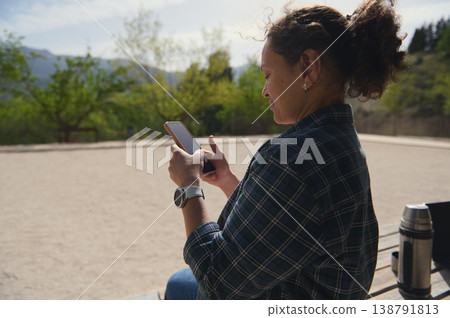 Woman using smartphone outdoors with mountain landscape, digital lifestyle concept 138791813