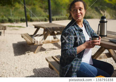 Woman with coffee sitting at picnic table outdoors with copy space Woman with coffee sitting at picnic table outdoors with copy space 138791838
