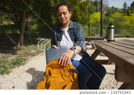Woman packing laptop into backpack after outdoor work Woman packing laptop into backpack after outdoor work 138791843