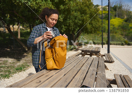 Woman packing backpack and thermos in park after work session Woman packing backpack and thermos in park after work session 138791850