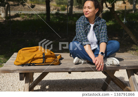 Woman sitting cross legged on table in park and looking away thoughtfully Woman sitting cross legged on table in park and looking away thoughtfully 138791866