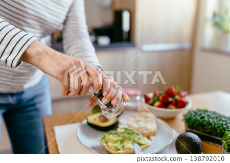 Middle aged woman hands adding pepper to avocado toast with microgreens strawberries and tea on table home kitchen healthy breakfast diet routine clean eating Middle aged woman hands adding pepper to avocado toast with microgreens strawberries and tea on table home kitchen healthy breakfast diet routine clean eating 138792010